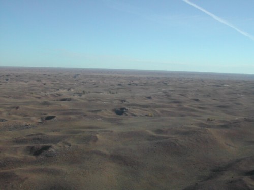 A vast, open landscape with rolling hills under a clear blue sky, stretching to the horizon.