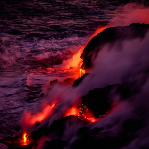 Lava flows into the ocean, creating steam and dramatic contrasts against dark rocks and waves.