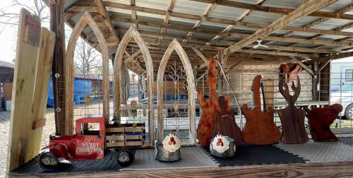 A rustic display featuring wooden sculptures, a vintage truck, and decorative arches under a covered structure.