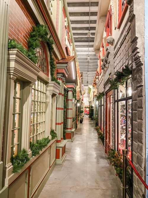 A festive indoor walkway lined with decorated storefronts and holiday greenery.