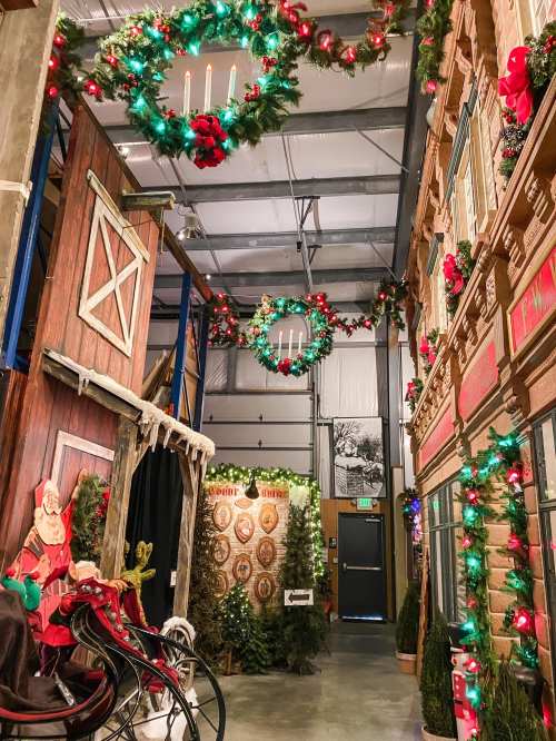 A festive indoor scene with holiday decorations, wreaths, and lights, featuring a barn and a vintage sleigh.