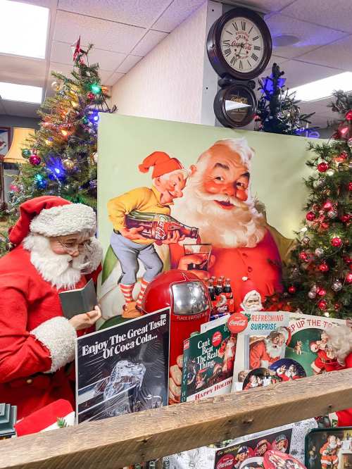 A festive scene with Santa Claus, a vintage Santa poster, Christmas trees, and holiday decorations.