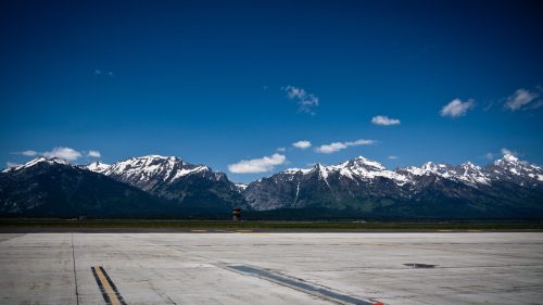 A clear blue sky above snow-capped mountains, viewed from an airport runway.