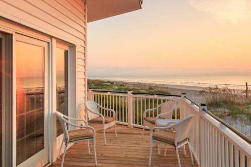 A serene beachside balcony at sunset, featuring two chairs and a view of the sandy shore and calm ocean.
