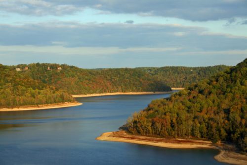 A serene landscape featuring a winding river surrounded by lush, colorful hills under a partly cloudy sky.