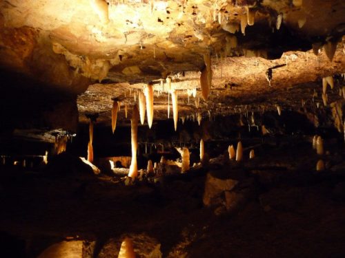 A dimly lit cave interior featuring stalactites and stalagmites, with rocky formations and a mysterious atmosphere.