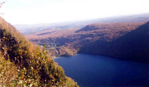 A scenic view of a lake surrounded by colorful autumn foliage and rolling hills under a clear sky.