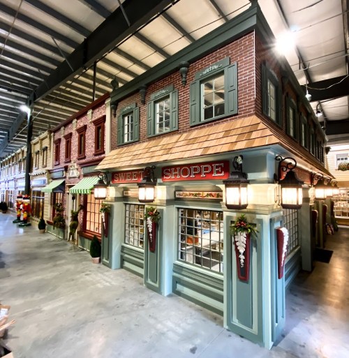 A charming miniature storefront with a "Sweet Shoppe" sign, featuring detailed brickwork and decorative lighting.