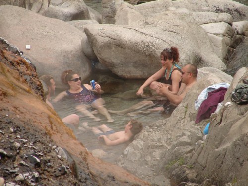 A group of people relaxes in a natural hot spring surrounded by rocks, enjoying the warm water and each other's company.