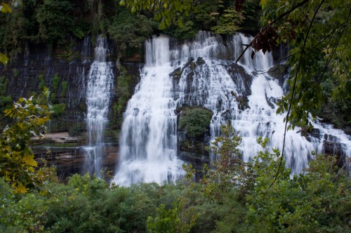 A cascading waterfall surrounded by lush greenery and trees, creating a serene natural landscape.