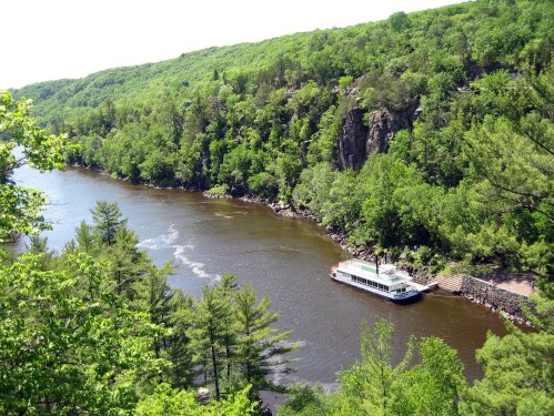 A scenic river view with lush green hills and a white boat docked along the shore.