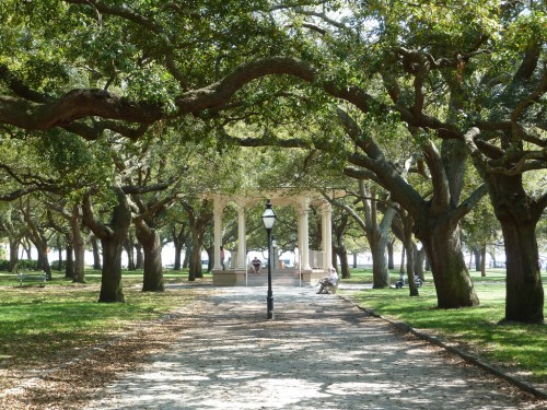 A serene park pathway lined with trees, leading to a gazebo under dappled sunlight.