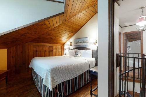 Cozy attic bedroom with a sloped wooden ceiling, a large bed, and warm lighting.