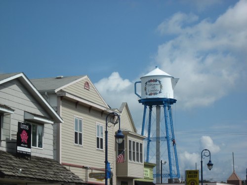 A blue water tower with "Follow Your Heart" painted on it, beside quaint buildings under a partly cloudy sky.