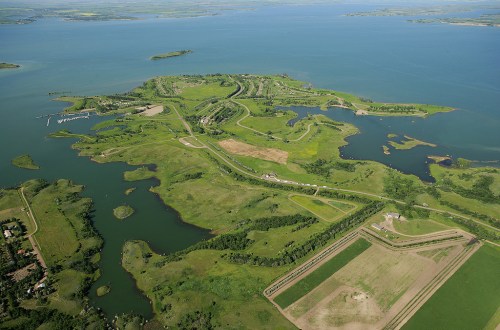 Aerial view of a lush green landscape with winding roads, water bodies, and islands under a clear blue sky.