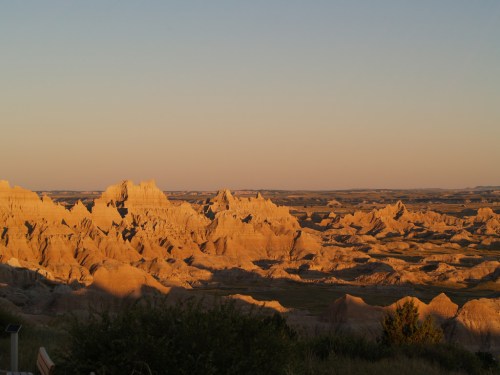 Golden-hued rock formations and rugged terrain under a clear sky at sunset in a vast landscape.
