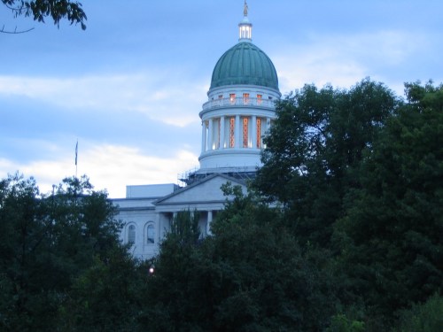 A historic building with a green dome, partially obscured by trees, under a cloudy sky at dusk.