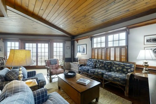 Cozy living room with wooden ceiling, plaid sofas, a coffee table, and large windows letting in natural light.