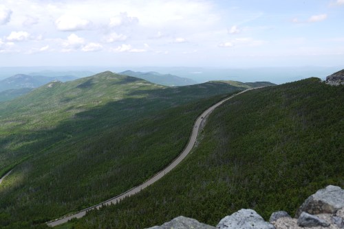 A winding road cuts through lush green mountains under a partly cloudy sky.