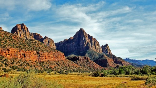 A scenic view of rugged red mountains under a blue sky, with green vegetation in the foreground.
