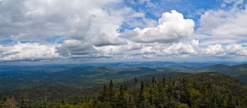 A panoramic view of lush green mountains under a blue sky filled with fluffy white clouds.