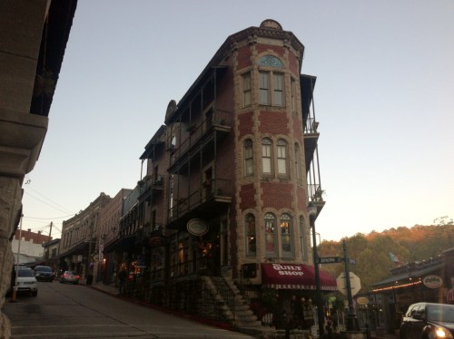 Historic brick building on a sloped street, featuring balconies and a shop on the ground floor.