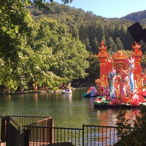 Colorful floating decorations on a lake, surrounded by lush greenery and hills in the background.