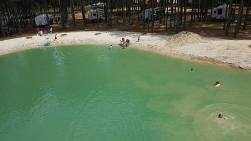 A serene green pond surrounded by trees, with people swimming and enjoying leisure activities on the shore.