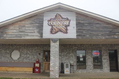 Exterior of a rustic country kitchen restaurant with a large sign, open sign in the window, and brick facade.