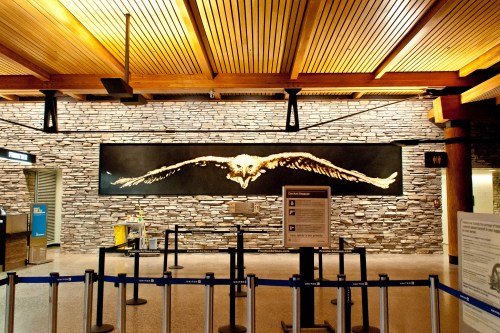 A large mural of an eagle with outstretched wings on a stone wall in an airport terminal.