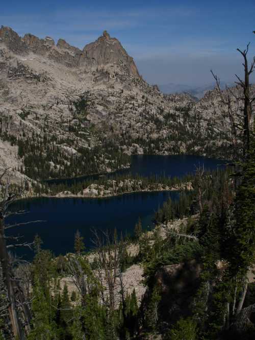 A scenic view of a mountain landscape featuring a deep blue lake surrounded by rugged terrain and evergreen trees.