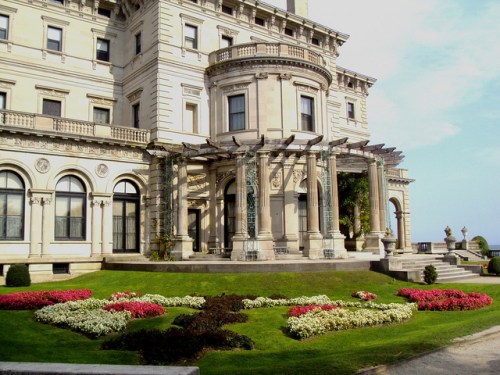 A grand mansion with ornate architecture, surrounded by colorful flower beds and lush green lawns.