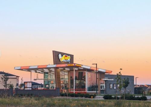 A modern fast-food restaurant with large windows, bright signage, and a colorful sunset in the background.
