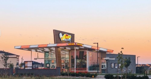 A modern fast-food restaurant with a colorful sign, large windows, and a sunset backdrop.
