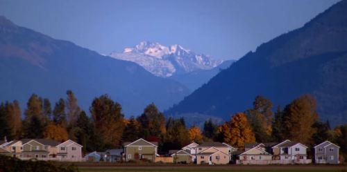 A scenic view of a small town with houses in the foreground and snow-capped mountains in the background.