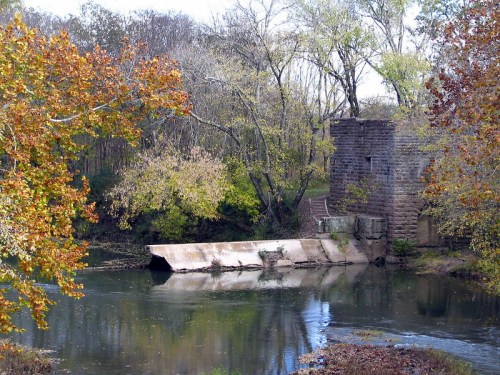 A serene river scene featuring a stone structure, surrounded by trees with autumn foliage reflecting in the water.