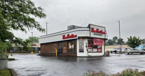 A Tim Hortons restaurant with a "Now Open" sign, surrounded by a parking lot on a cloudy day.