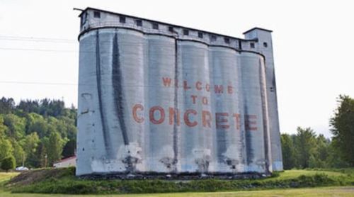 A large, weathered grain silo with "WELCOME TO CONCRETE" painted on the side, surrounded by greenery.