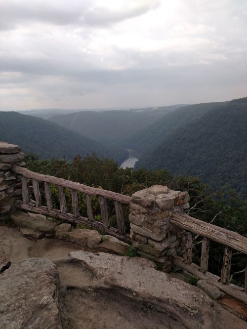 A scenic view of a river winding through lush green mountains, framed by a rustic wooden railing.