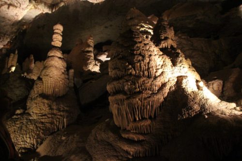 Stalactites and stalagmites illuminated in a dark cave, creating a dramatic natural landscape.