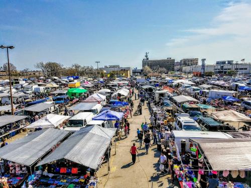 Aerial view of a bustling outdoor market with numerous tents, vendors, and shoppers under a clear blue sky.