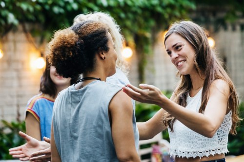 Two women engage in a friendly conversation outdoors, surrounded by greenery and warm lighting.
