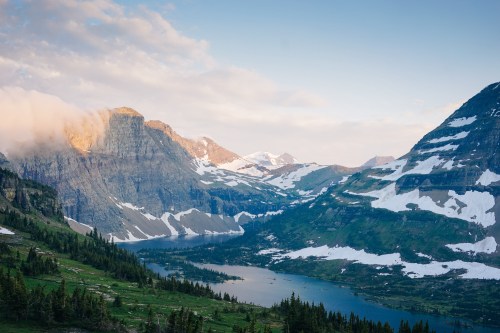 A scenic view of mountains and a lake, with snow-capped peaks and lush green valleys under a partly cloudy sky.