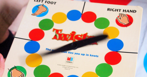 A close-up of a Twister game spinner, showing colored circles and instructions for left foot and right hand.