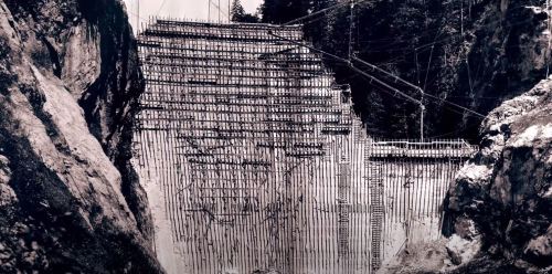 A black and white image of a steep, rocky slope supported by wooden scaffolding and cables.