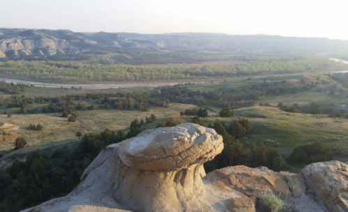 A scenic view of rolling hills and a river, featuring a unique rock formation in the foreground.