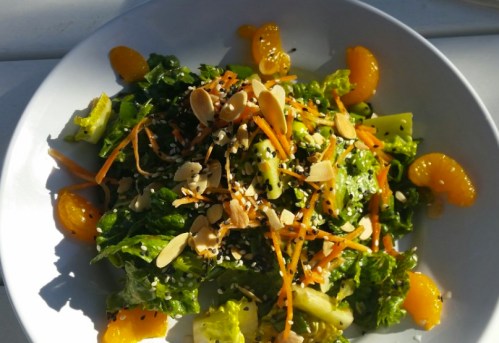 A vibrant salad with greens, mandarin slices, carrots, almonds, and sesame seeds in a white bowl.