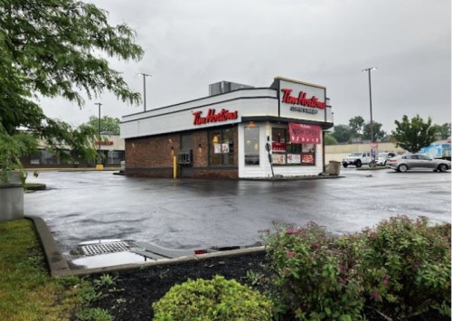 A Tim Hortons restaurant on a rainy day, surrounded by a parking lot and greenery.