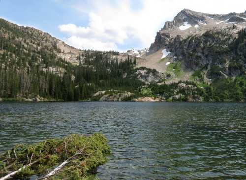 A serene lake surrounded by mountains and lush greenery under a partly cloudy sky.