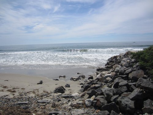 A serene beach scene with gentle waves, rocky shore, and a clear blue sky.